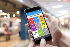 Photo of two hands holding a smartphone, with the colorful tiles of the DAKS Mobile Client visible on the screen