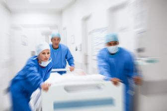 Doctors in blue surgical gowns rush down the hallway with a hospital bed.
