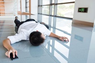 Mann liegt bäuchlings auf dem Boden eines Flurs mit einem Smartphone in der rechten Hand