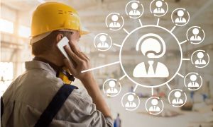 Arbeiter mit gelbem Schutzhelm telefoniert, daneben Schema von mehreren Konferenzteilnehmern