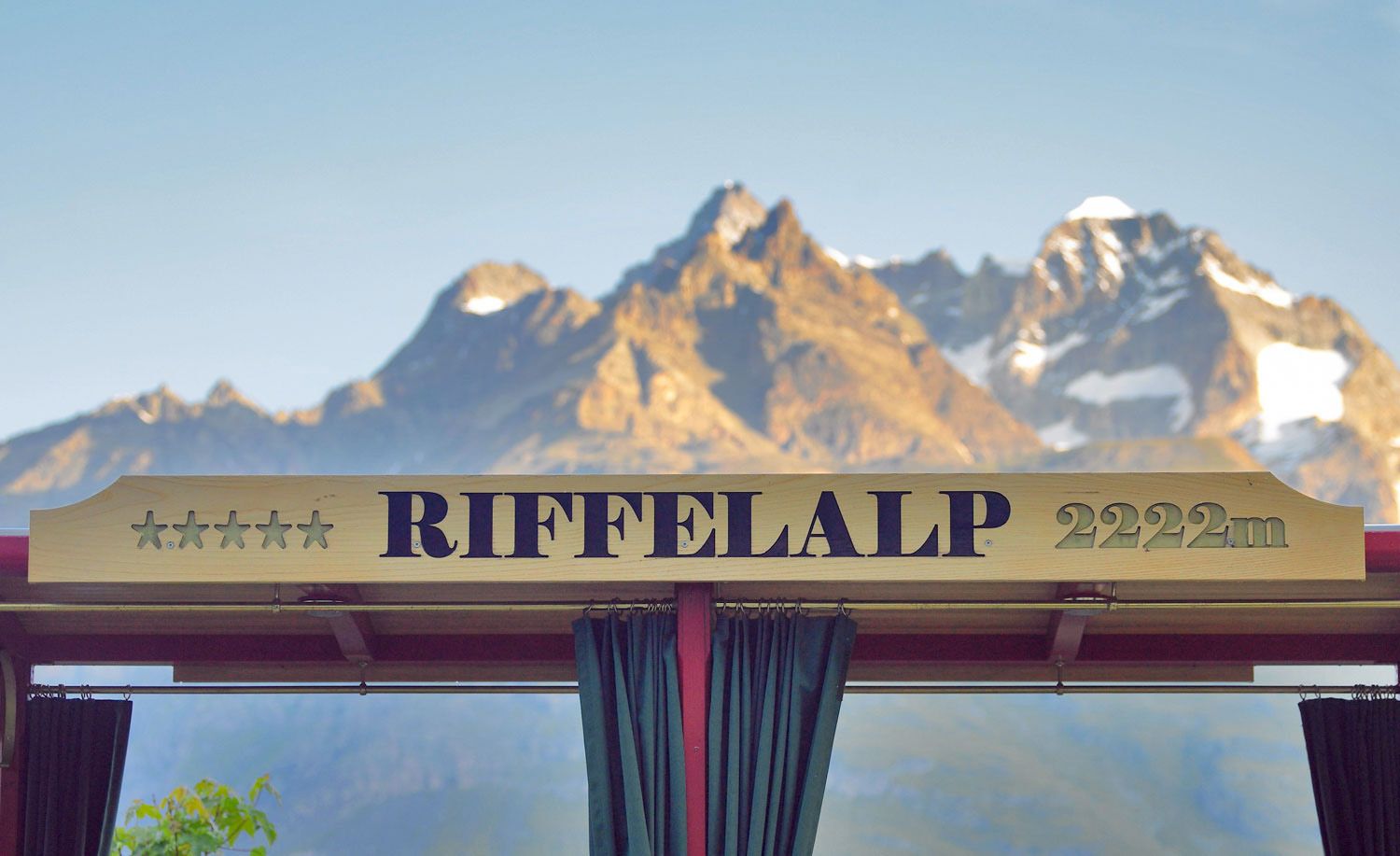 Sign reading "Riffelalp" in front of a beautiful mountain scenery