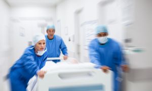 Doctors in blue surgical gowns rush down the hallway with a hospital bed.